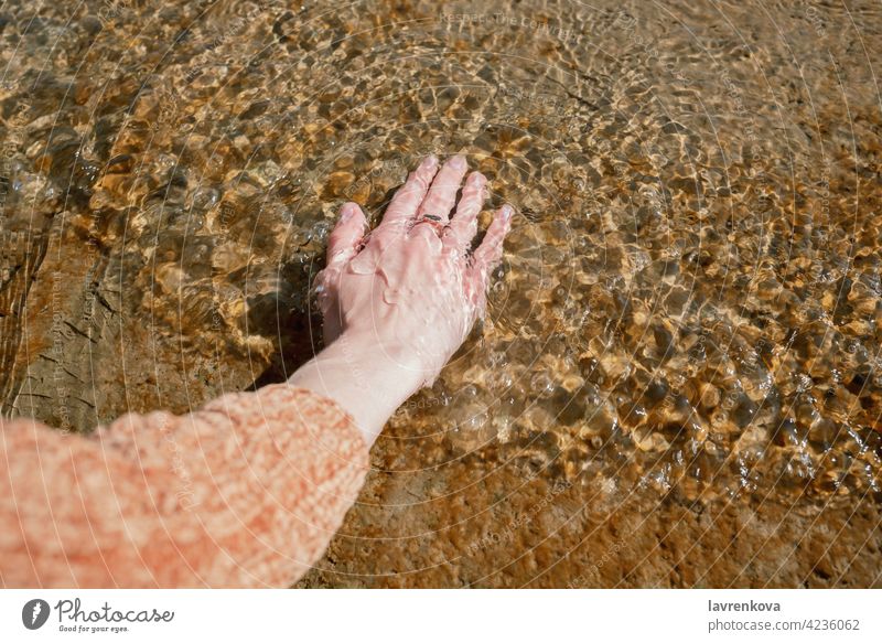 Woman's hand in the cold water on a pier female faceless beach touching element clean clear sweater ripple nature outdoors peaceful lake lifestyle sea river