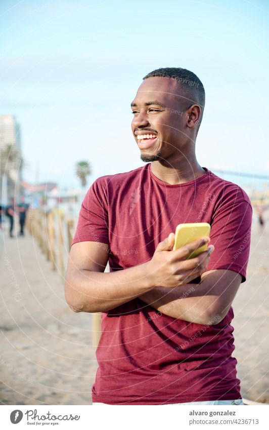 young black man at the beach smiling and using his smartphone african male american adult portrait model cellphone handsome casual attractive che person