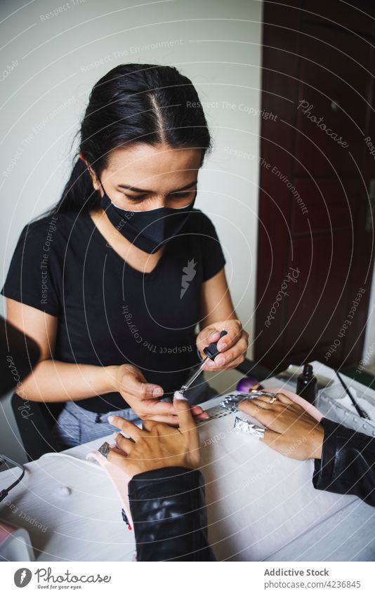 Female master using foil while doing manicure for client in salon women gel nail polish remove beauty care procedure treat spa service table professional
