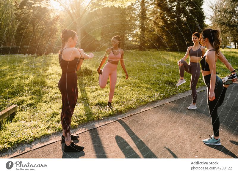 Multiethnic sportswomen warming up on walkway in city park warm up stretch training workout leg raised exercise multiracial footpath asphalt together sportswear