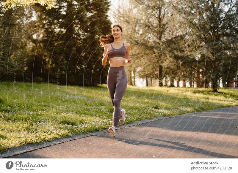 Smiling runner jogging on walkway in park sport cardio training workout activity smile woman road asphalt sportswoman exercise practice cheerful content fast