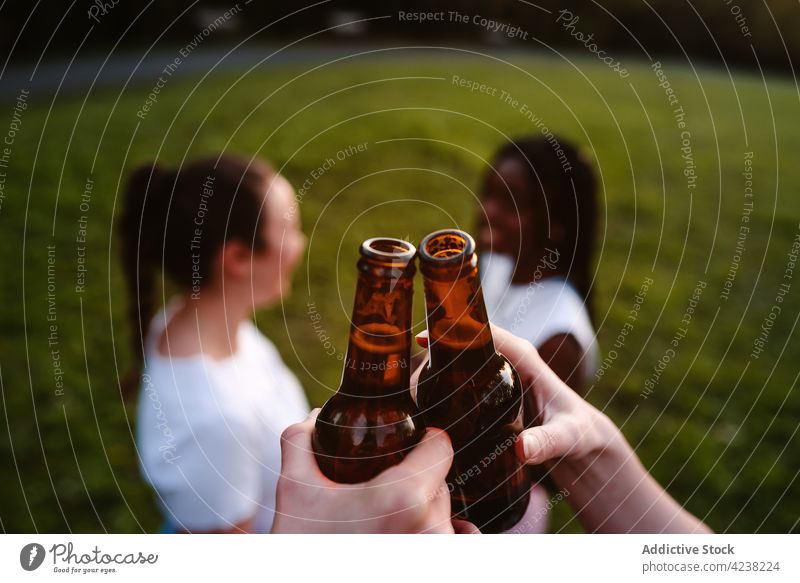Company of multiracial female friends clinking bottles in park at sunset women company summer beer chill having fun multiethnic diverse black african american