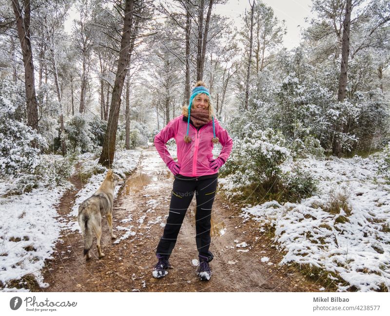 Caucasian young woman with a wolf dog enjoying snow outdoor in a path in a forest area in winter time. lifestyle people style of life wanderlust hiker caucasian