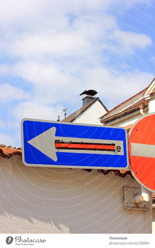 Street signs in front of wall and houses Road sign Signs and labeling Transport Road traffic Wall (barrier) pasted over Red Blue White Arrow