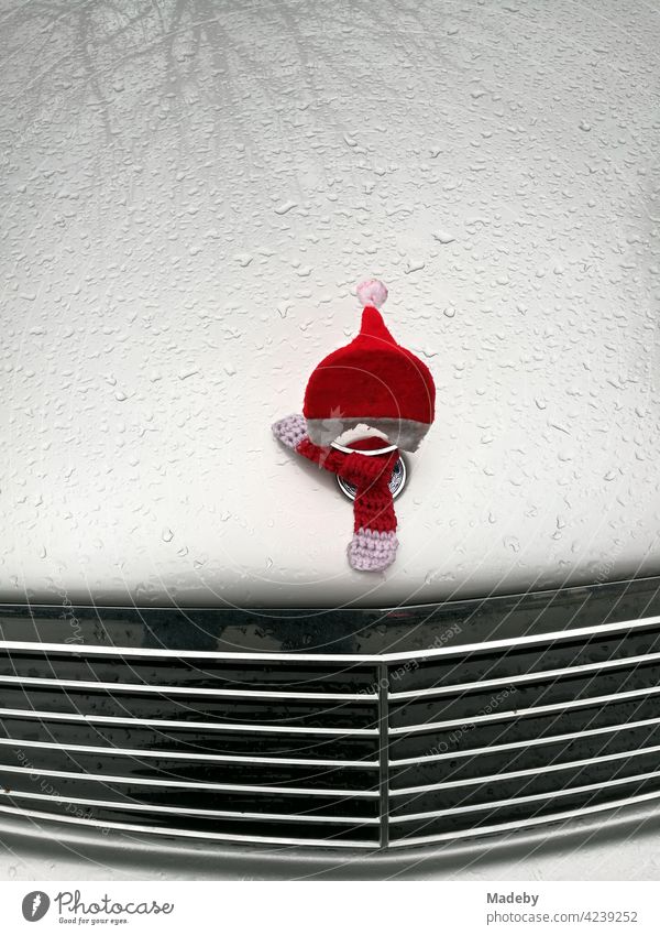Kostüm eines Weihnachtsmann mit Zipfelmütze auf der Kühlerfigur einer berühmten deutschen Automarke mit Kühlergrill und Regentropfen auf der Motorhaube in Lemgo bei Detmold in Ostwestfalen-Lippe