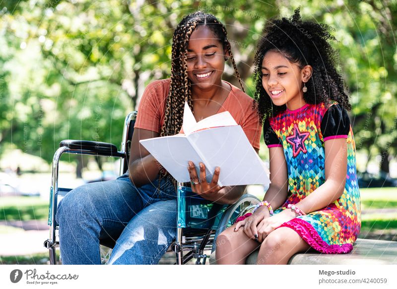 Woman in a wheelchair reading a book with her daughter. park woman disabled black together outdoor care lifestyle day cheerful leisure enjoying kid child