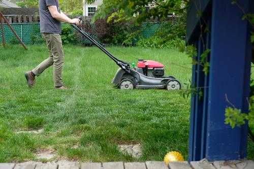 Man mowing tall grass; suburban back yard with deck and landscaping lawn mower lawnmower growth chore weekend exercise home wood garden work green gardening cut