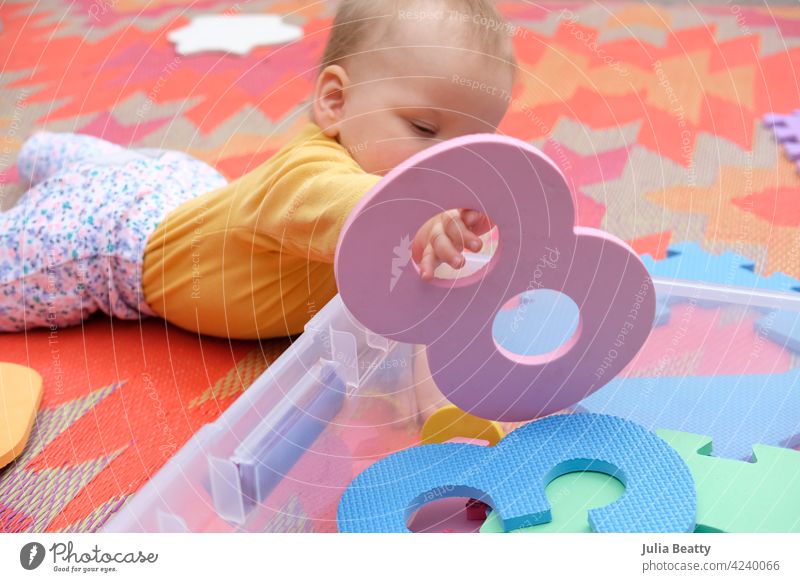 Crawling baby playing with foam number tiles on a colorful outdoor rug; holding number 8 foam tiles numbers mat puzzle tummy time crawl scoot lay down reaching