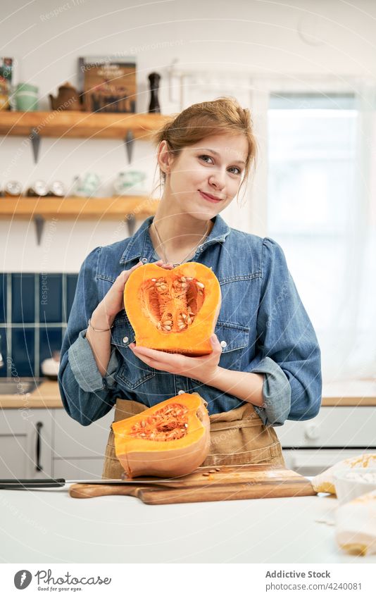 Smiling woman showing cut pumpkin at table in kitchen vegetable vegan smile cook vitamin portrait satisfied content cheerful half seed pulp squash raw