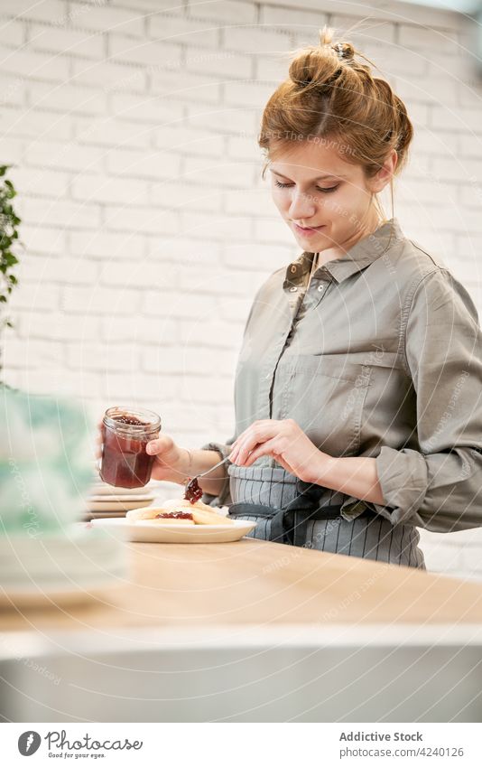 Smiling woman putting tasty jam on pancakes at home berry dessert treat sweet breakfast cook kitchen delicious smile jelly marmalade enjoy loft style brick wall