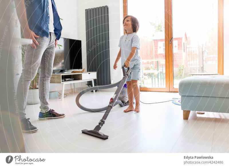 Boy vacuuming floor while father standing at home vacuum cleaner helping chores homework learning indoors house man dad family parents relatives son boy kids