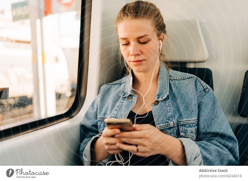 Woman listening music and browsing phone in train woman ride commute earphones smartphone passenger transport social media using mobile window young lifestyle