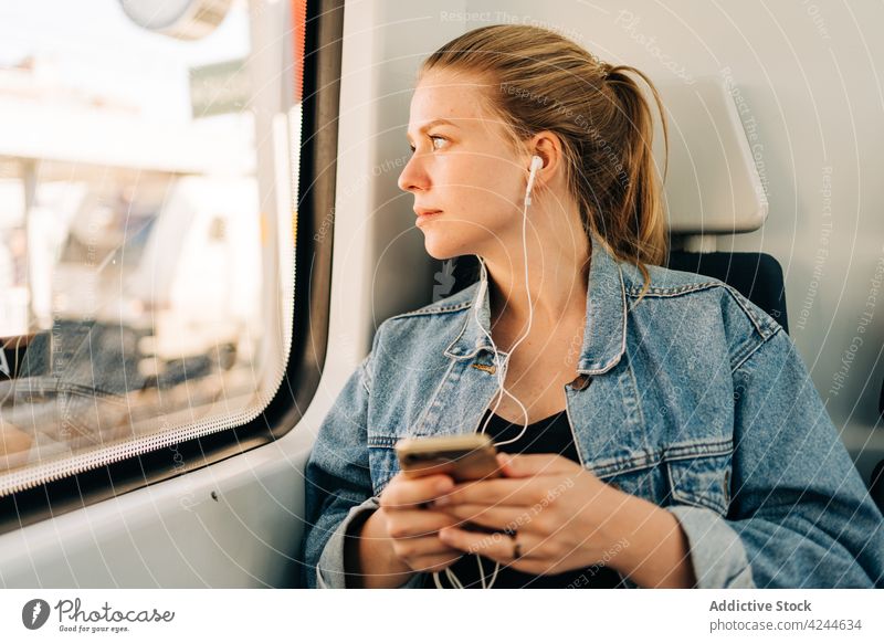 Woman listening music and looking away in train woman ride commute earphones smartphone passenger transport social media using mobile window young lifestyle