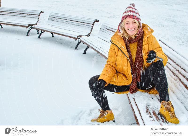 Caucasian young woman sitting on a bench enjoying snow outdoor in winter time. lifestyle people style of life weather charming happy feelings caucasian female