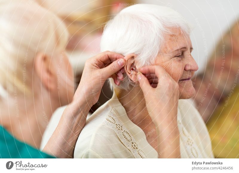 Nurse places a hearing aid in the senior woman's ear Deafness examine listening adjusting audio equipment close up hand audiologist applying hearing loss nurse