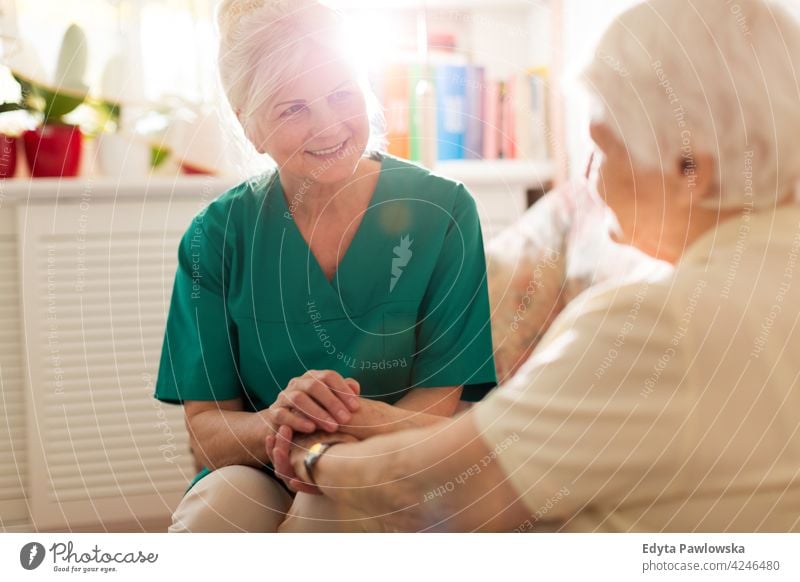 Nurse consoling her elderly patient by holding her hands people woman senior mature casual female Caucasian home house care health healthcare nursing home aging
