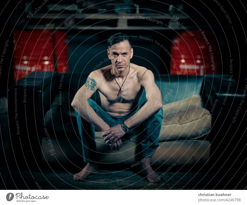 man sits on sofa in auto repair shop Man portrait Naked shirtless naked torso jeans Barefoot Auto repair shop Sofa Jewellery Cool Advertising work sexy erotic