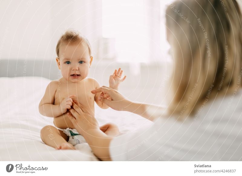 A young mother smears the baby's tummy with baby cream. Child care, childhood, parenting mom skin infant toddler small hand massage white health hygiene newborn