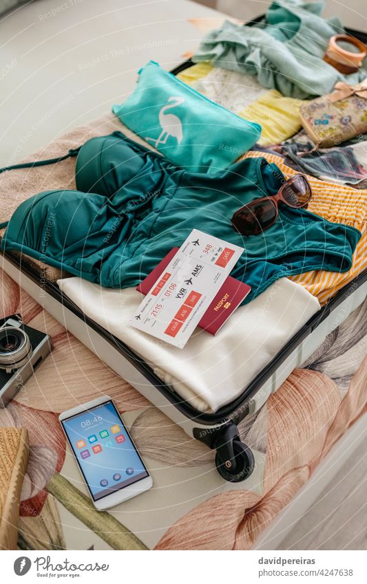 Open woman suitcase prepared for summer vacation top view boarding pass passport open suitcase baggage preparation swimsuit mobile beach holiday travel clothes