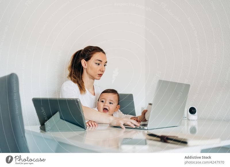 Mother using laptop and baby watching cartoons on tablet mother together desk work browsing happy childcare at home babyhood woman self employer motherhood