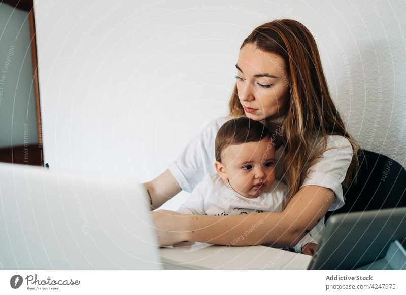 Mother using laptop and baby watching cartoons on tablet mother together desk work browsing happy childcare at home babyhood woman self employer motherhood