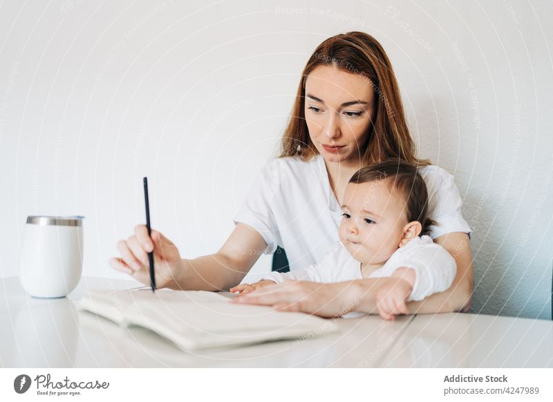 Mother writing on diary while holding cute baby mother write take note copybook together attentive casual sit concentrate woman education adorable focus care