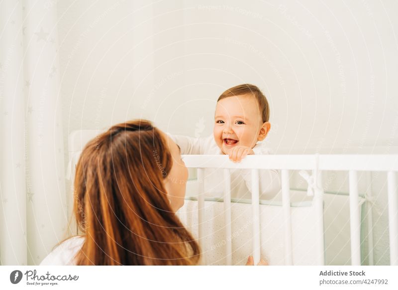 Mother sitting near cute laughing baby in cradle mother happy joyful motherhood offspring childcare crib adorable parent parenthood woman toddler innocent