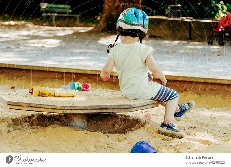 Child with bicycle helmet sits in sandbox on playground Playing Sandals Sandpit Playground Infancy Exterior shot Colour photo Kindergarten Toddler Toys