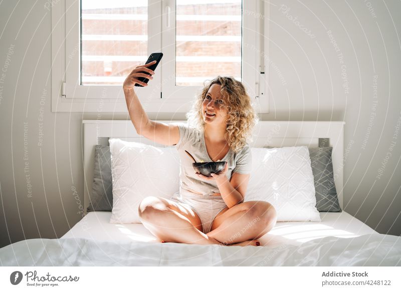Content woman taking photo of meal and sitting on bed take photo smartphone selfie self portrait breakfast content morning glad yummy eat delicious enjoy