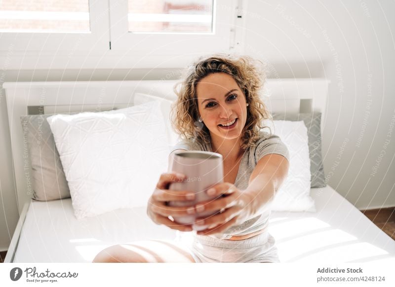 Happy woman outstretching arms with cup in bedroom toothy smile happy cheerful morning hot drink comfort content glad sit cozy lifestyle positive mug relax joy