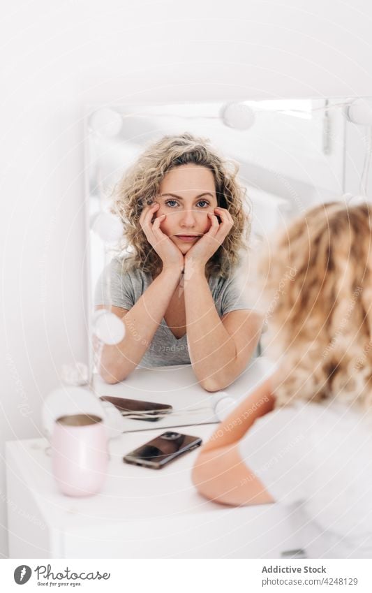 Calm woman touching face and looking in mirror attentive reflection touch face vanity bedroom calm thoughtful appearance observe feminine unemotional