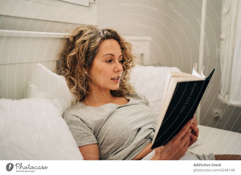 Woman reading book while lying on bed woman rest home happy comfort bookworm lazy weekend relax delight female young curly hair morning chill bedroom cozy calm