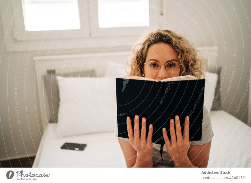 Happy young woman reading novel while resting on bed book smile free time hobby bookworm interesting relax happy female curly hair blond eyeglasses panties