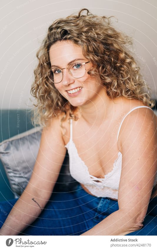 Smiling young woman leaning on couch sitting on sofa at home relax smile positive style confident happy cozy apartment comfort content female curly hair blond