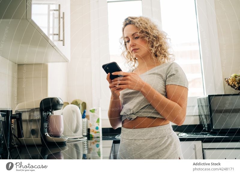 Calm woman using smartphone in kitchen browsing calm domestic at home gadget cellphone device casual mobile connection online surfing modern internet