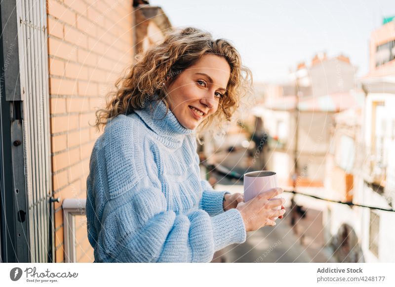 Smiling young female drinking coffee on balcony woman smile style enjoy beverage morning relax home hot cozy curly hair blond chill comfort happy content aroma