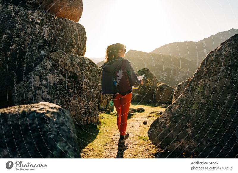 Anonymous woman reading map amidst rocky formations during hiking trip boulder traveler hike walk trekking smile orientate happy female young casual brunette