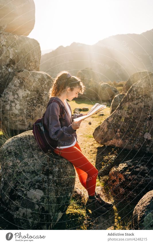 Cheerful young woman reading map amidst rocky formations during hiking trip boulder traveler hike trekking smile orientate happy female casual brunette vacation