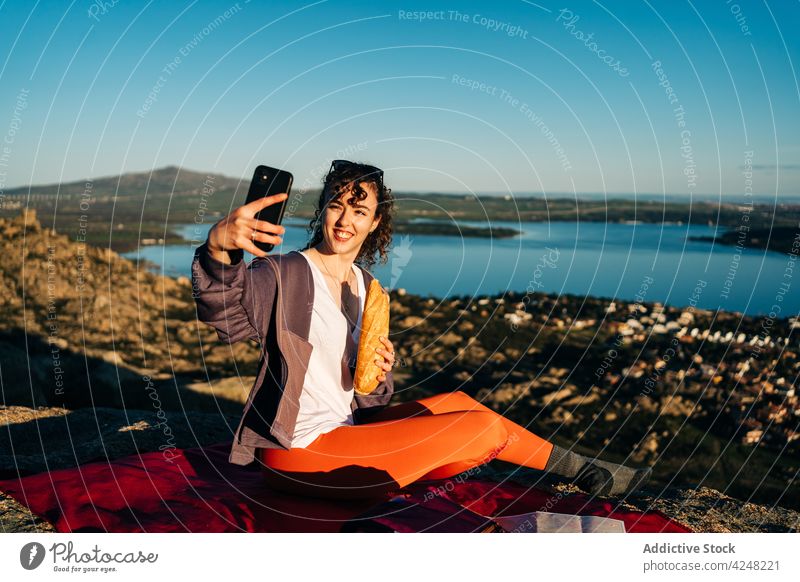 Traveling woman having picnic and taking photo with smartphone on rocky mountain eat sandwich selfie hiker sea happy travel relax trekking nature mobile food