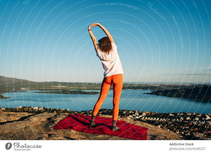 Anonymous woman practicing yoga on rocky mountain over sea stretch warm up nature mindfulness stress relief wellness harmony healthy calm female young