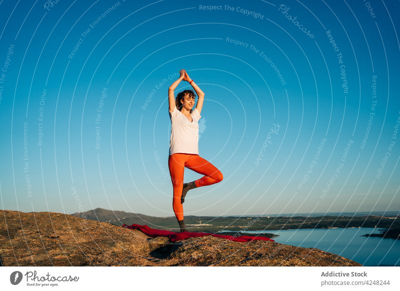 Woman practicing Vrksasana pose during yoga session in nature woman vrksasana tree with arms up balance zen mindfulness mountain wellness practice harmony