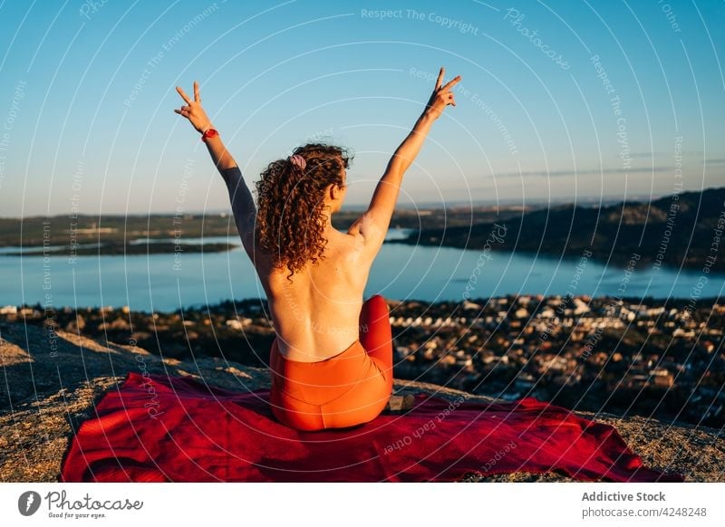 Fit topless woman showing V sign with raised arms on rocky mountain v sign happy traveler smile joy content positive town tourist enjoy female young curly hair