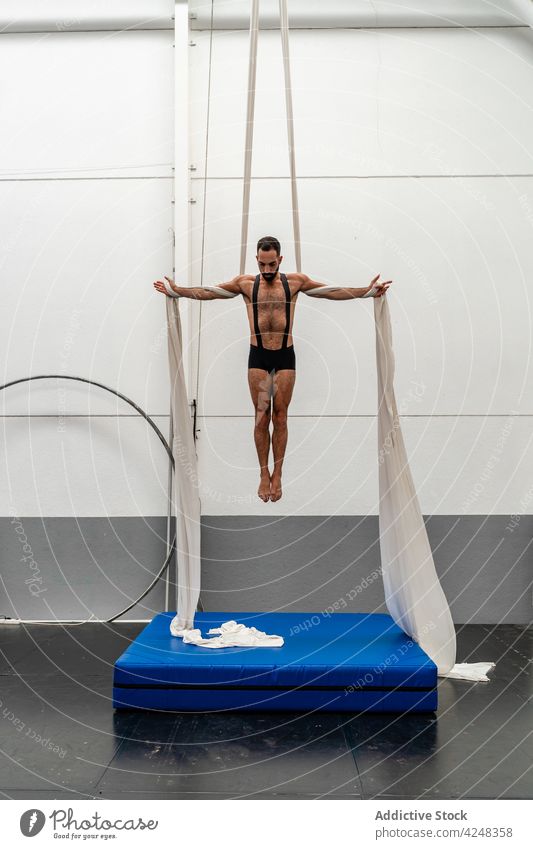 Focused sportsman hanging on aerial silks skill training strong exercise fit workout above ground fitness gym effort strength physical energy motivation