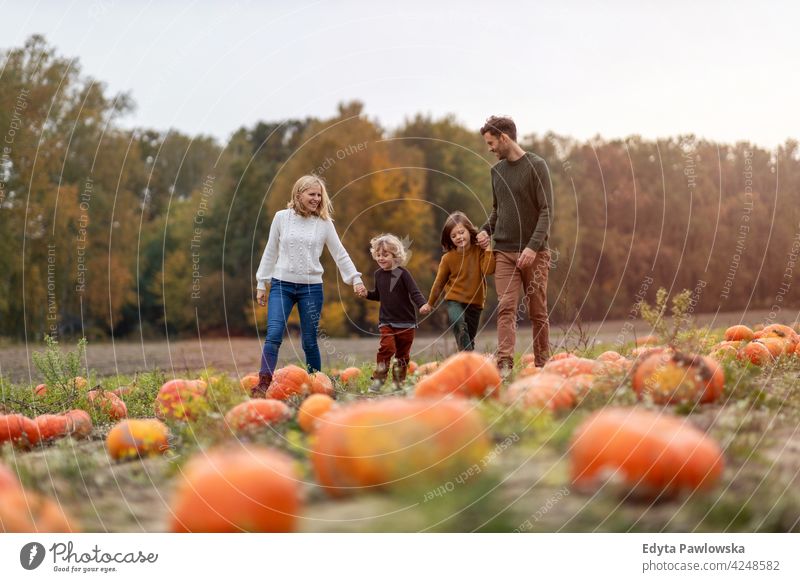 Happy young family in pumpkin patch field halloween nature park autumn fall man dad father woman female mother parents relatives son boy kids children