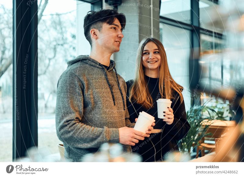 Friends doing shopping in a coffee shop. Young man and woman having chat while picking out the pastry, bakery's goods and hot drinks standing at counter in a coffee shop. People buying coffee and sweet snacks to go