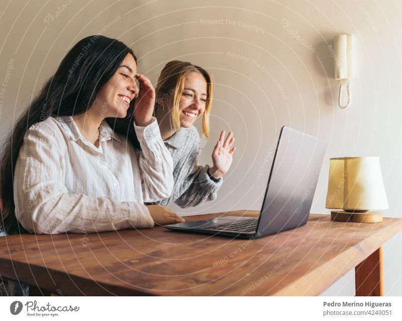 two women friends waving while on video call laptop woman lifestyle internet sitting computer happy together couple love home young online technology adult