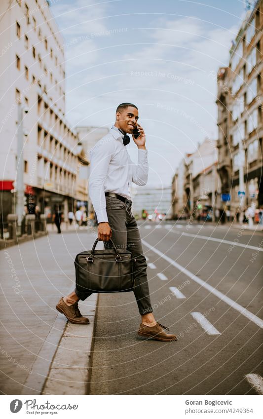 Young African American businessman using a mobile phone while crossing a street american black building cab call calling causal city communication downtown