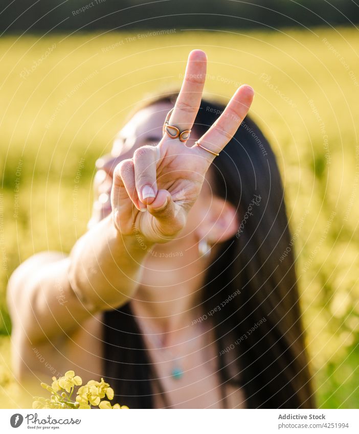 Smiling woman showing v sign on blooming field two fingers toothy smile cheerful gesture nature happy peace joy positive young expressive brunette summer