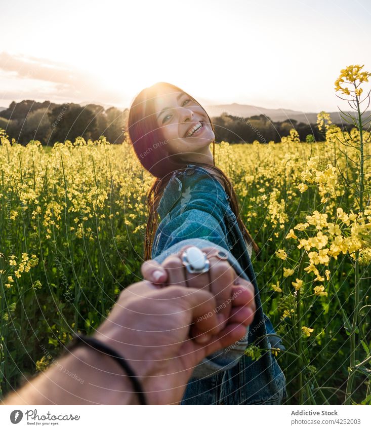 Joyful woman holding boyfriend hand and standing on blooming field couple follow me joyful holding hands toothy smile cheerful romantic together countryside