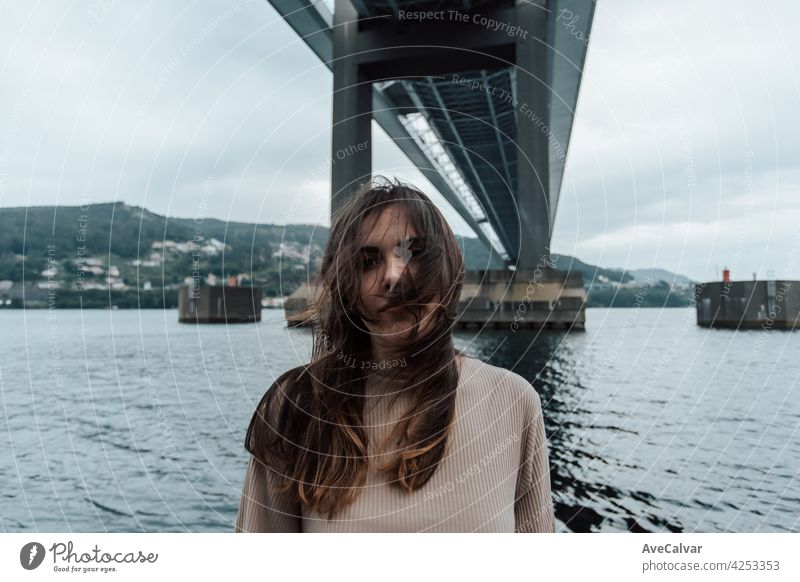 Portrait under a bridge of a woman moving his hair, time stop, mental health concept with copy space, modern sea, relax person anxiety emotion frustration